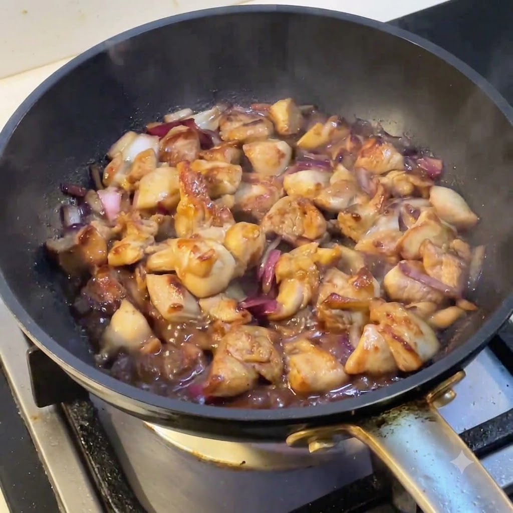 表面から湯気が立ち上る、鶏肉と玉ねぎが煮込まれているフライパン。
