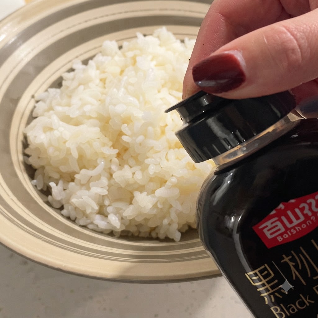 ボウルに盛られたふっくらとした白飯の上に、ボトルから黒トリュフソースを垂らしている様子。