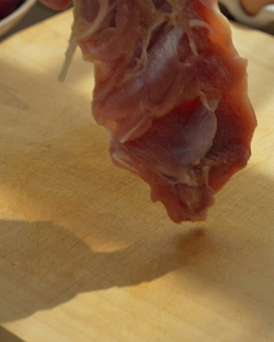 木のまな板の上で鶏もも肉を包丁で切っている様子。
