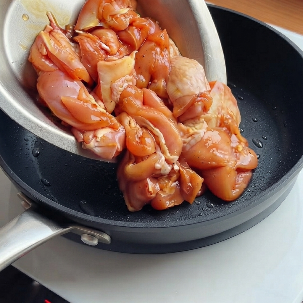 下味をつけた鶏肉を熱したフライパンに入れて香ばしく炒める様子。