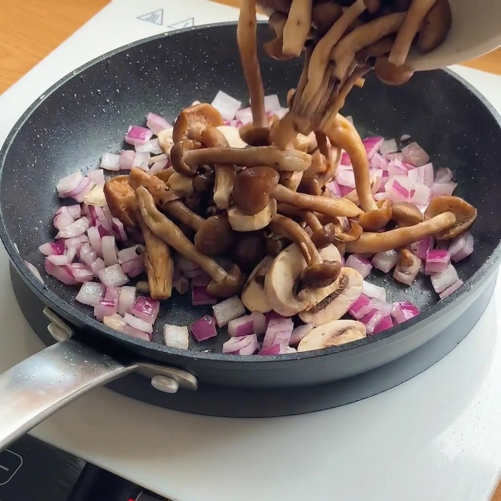 焼いた鶏肉が入ったフライパンにスライスしたマッシュルームと赤玉ねぎを加える様子。