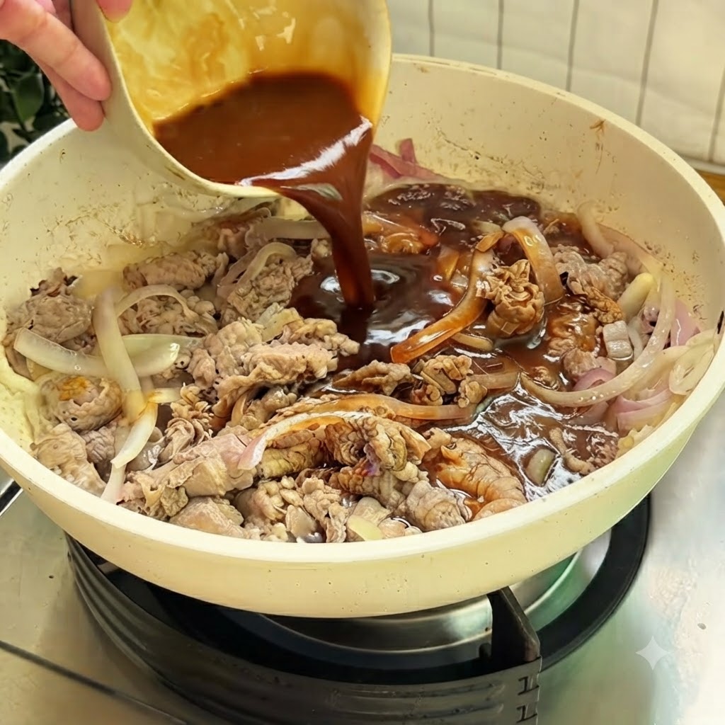 牛肉と玉ねぎの入った白いフライパンに、小さなボウルから濃厚な茶色のタレを注いでいる様子。