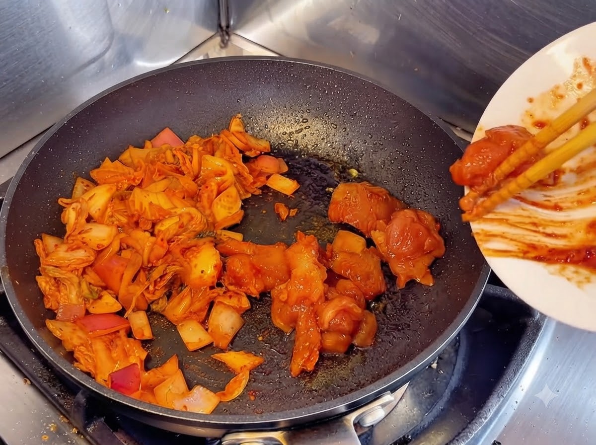 炒めたキムチと玉ねぎの隣にあるフライパンに、白い皿からマリネした生の鶏肉の塊を箸で滑り込ませている様子。