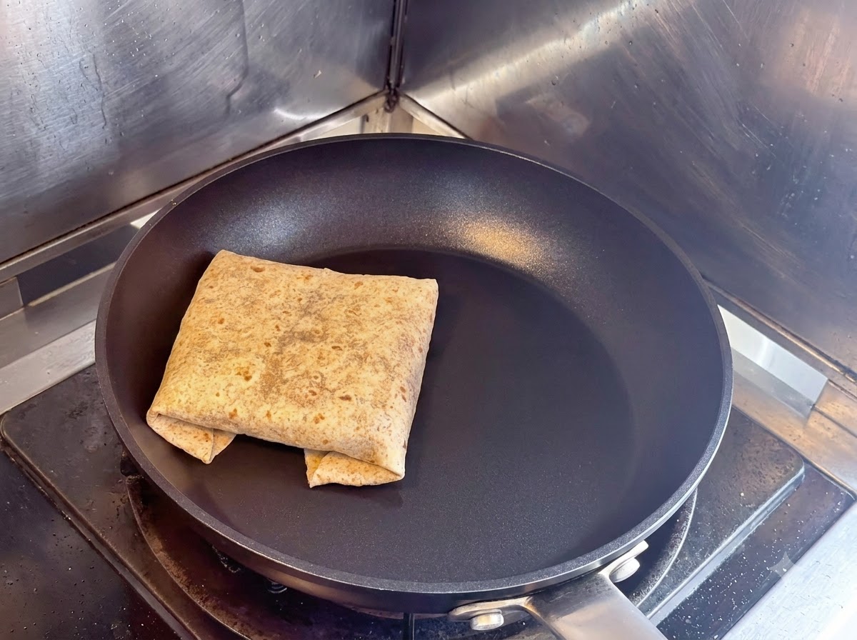 乾いた黒いノンスティックのスキレットの中で、折り目を下にして焼かれている四角いフラットブレッドのラップ。