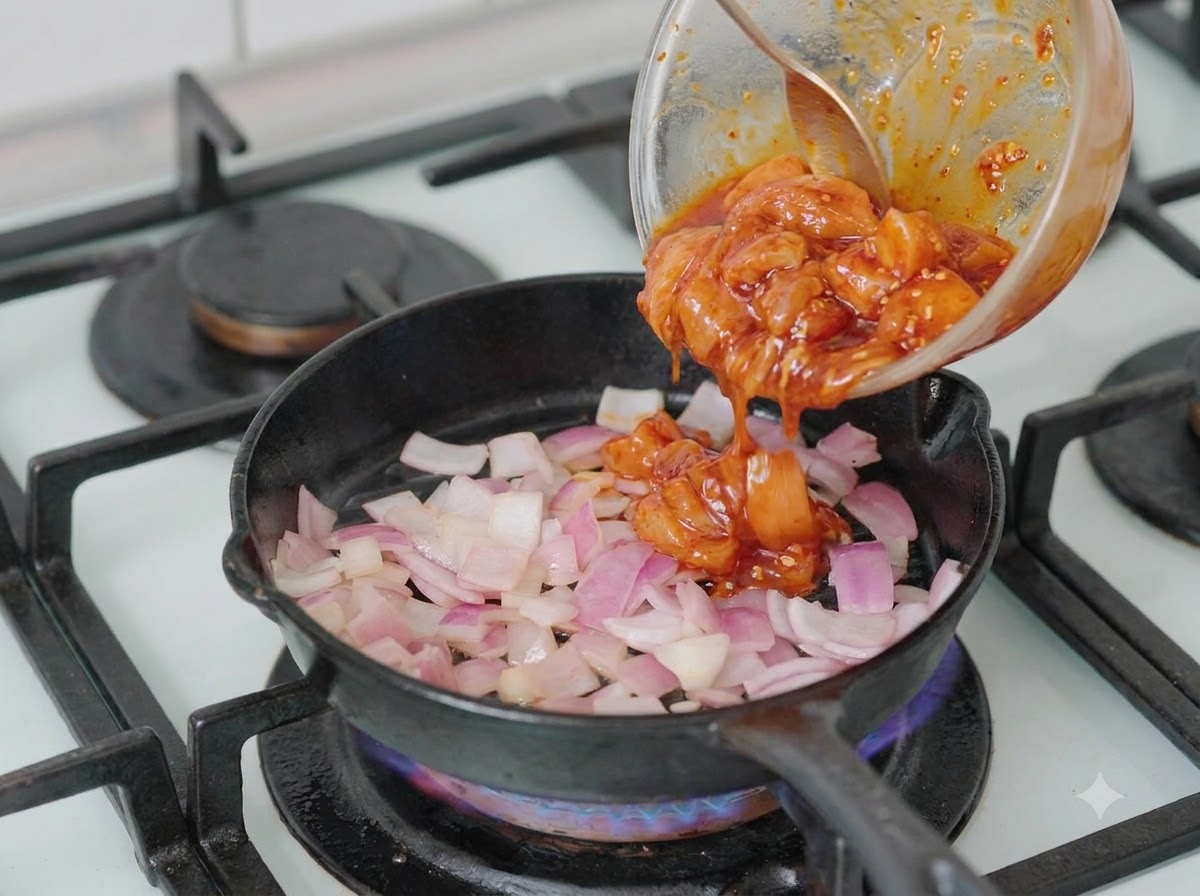 刻んだ玉ねぎが入ったフライパンに、ボウルからマリネした鶏肉を入れている様子。