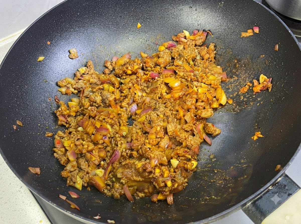 フライパンの中のカレーと肉のソースに、牛乳を注ぎ入れている様子。