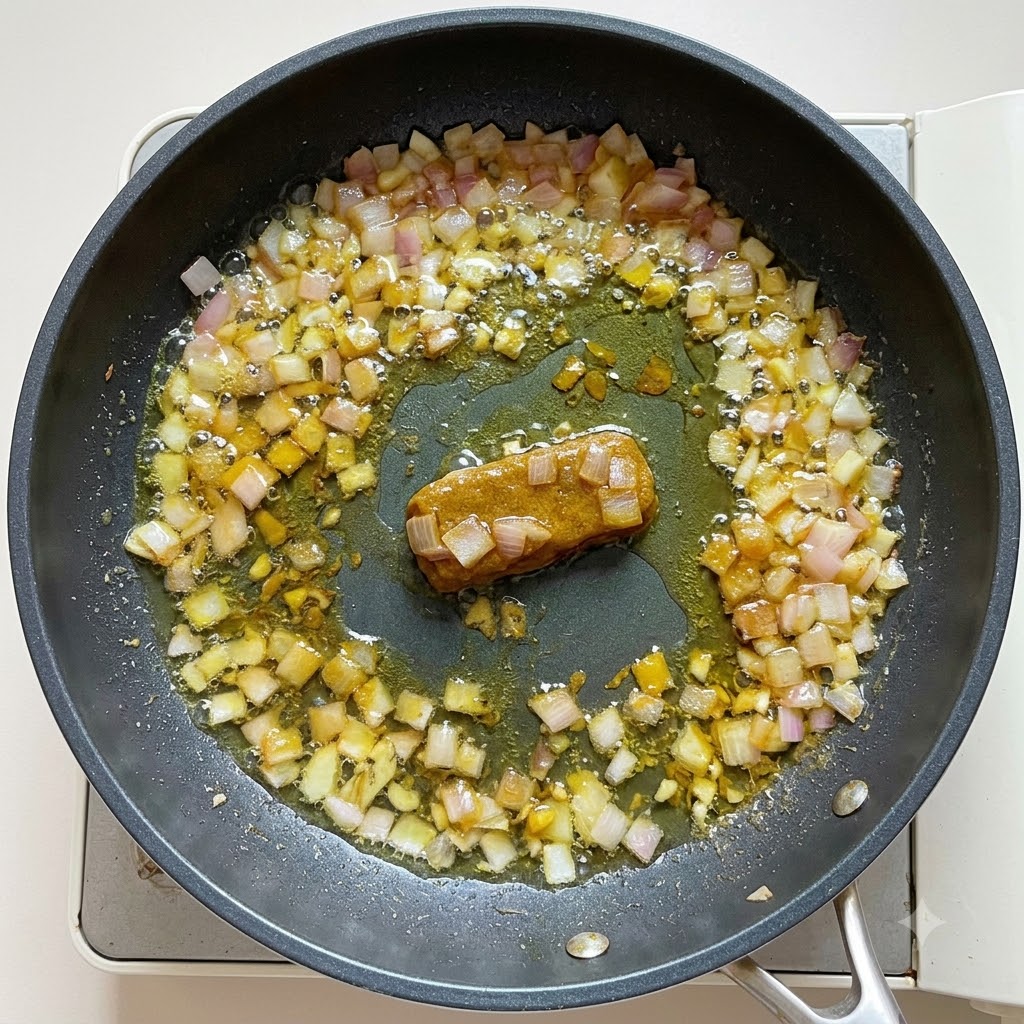 フライパンでカレーのベースに水とココナッツミルクを注ぎ、とろみがつくまでかき混ぜている様子。cite: 1