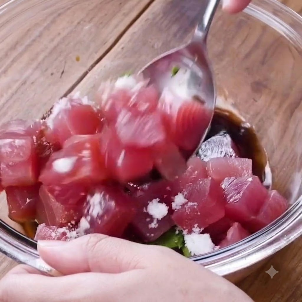ガラスボウルの中で、スプーンを使って角切りのマグロとアボカド、調味料を優しく混ぜ合わせているところ。