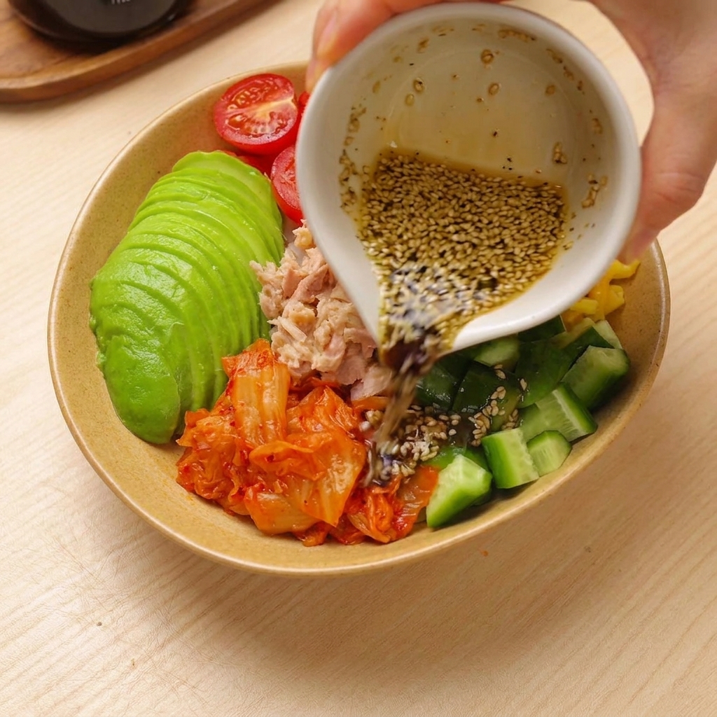 色鮮やかに盛り付けられたツナアボカド丼にドレッシングをかけている様子。