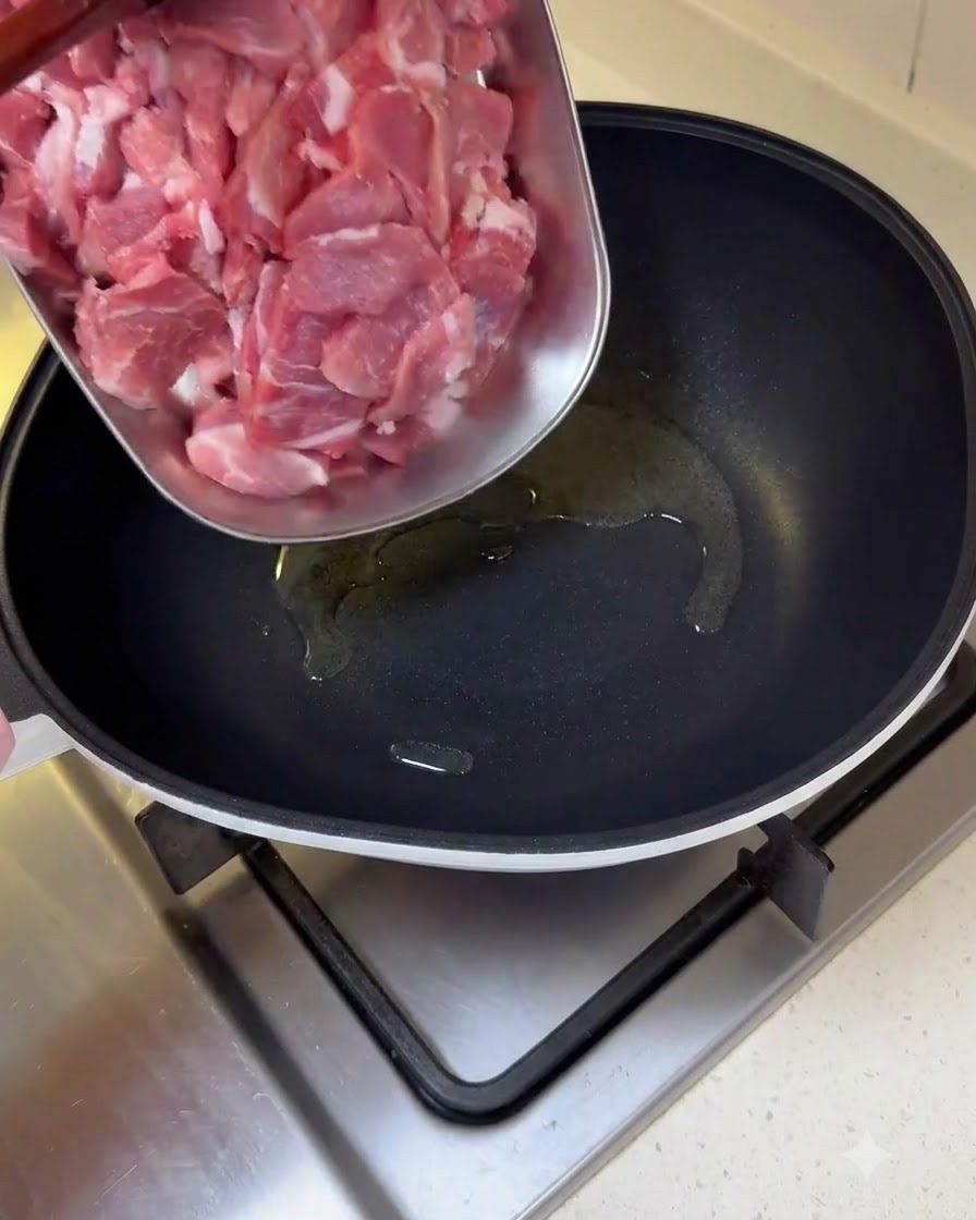 トレイからスライスした生の豚肉を、油をひいたフライパンに移している様子。