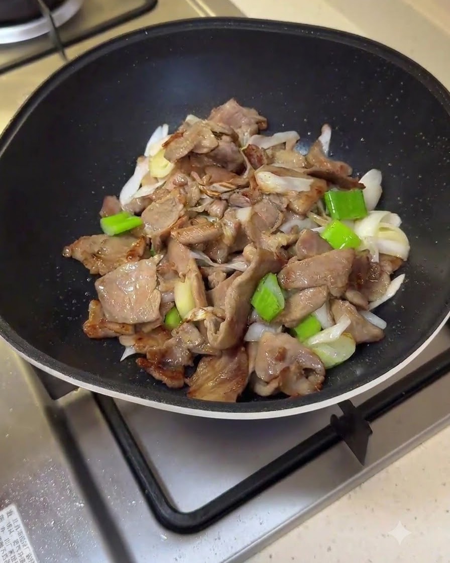 豚肉と長ネギが入ったフライパンに、赤いソースの混合物を注いでいる様子。