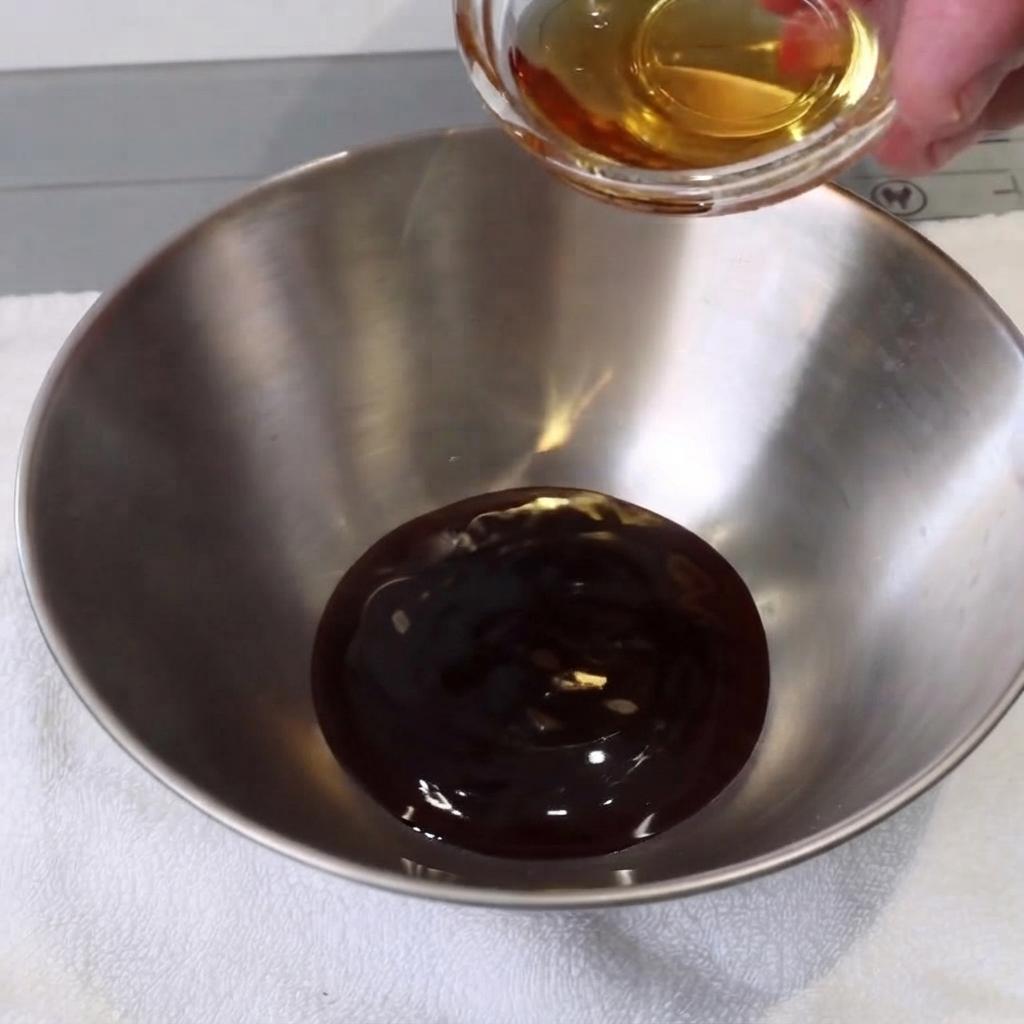 白いタオルの上にある小さな金属製のボウルで、スプーンを使って液体状の材料が混ぜられている様子。