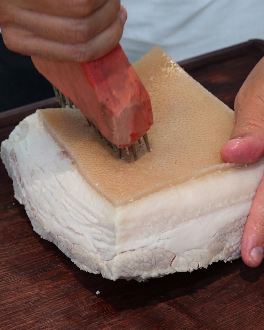 肉用刺し器を使って、豚肉の皮の表面に繰り返し穴を開けているクローズアップ。