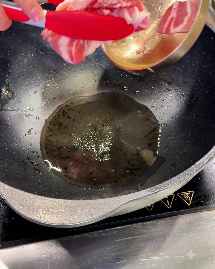 赤いトングを使って、熱した油を入れた中華鍋に豚バラ肉のスライスを入れている様子。