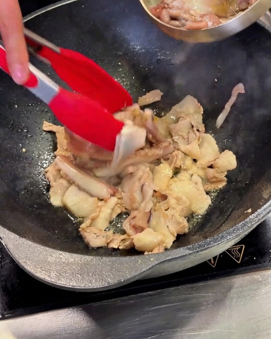 下処理したイカの切り身を、豚バラ肉の入った中華鍋にステンレスのボウルから移している様子。