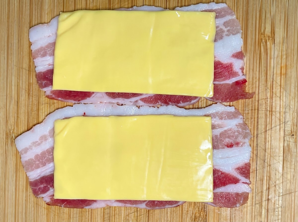 絞り袋に入ったエビすり身が、チーズを乗せた豚バラ肉の層の上に絞り出されている様子。