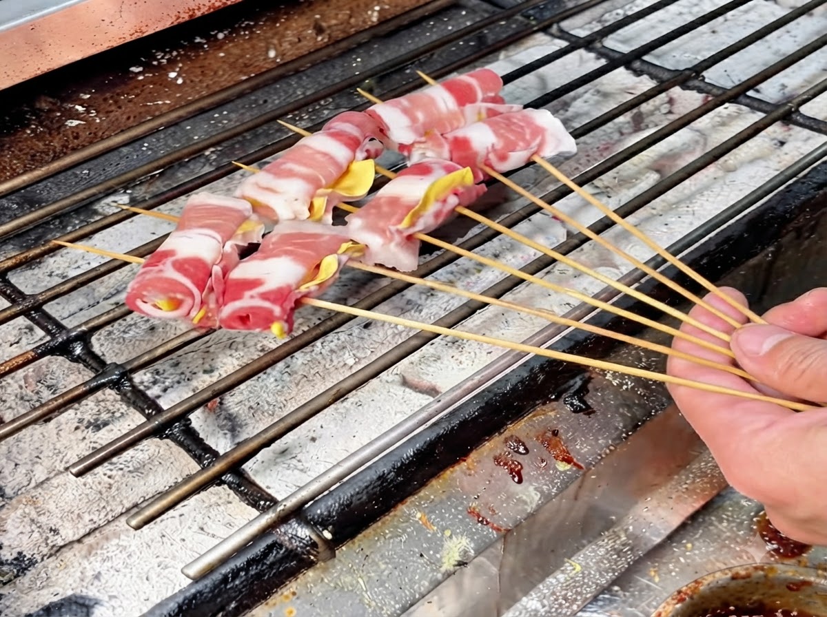 じっくり焼くために、熱い炭火のグリル網の上に並べられた複数の肉巻きの串。