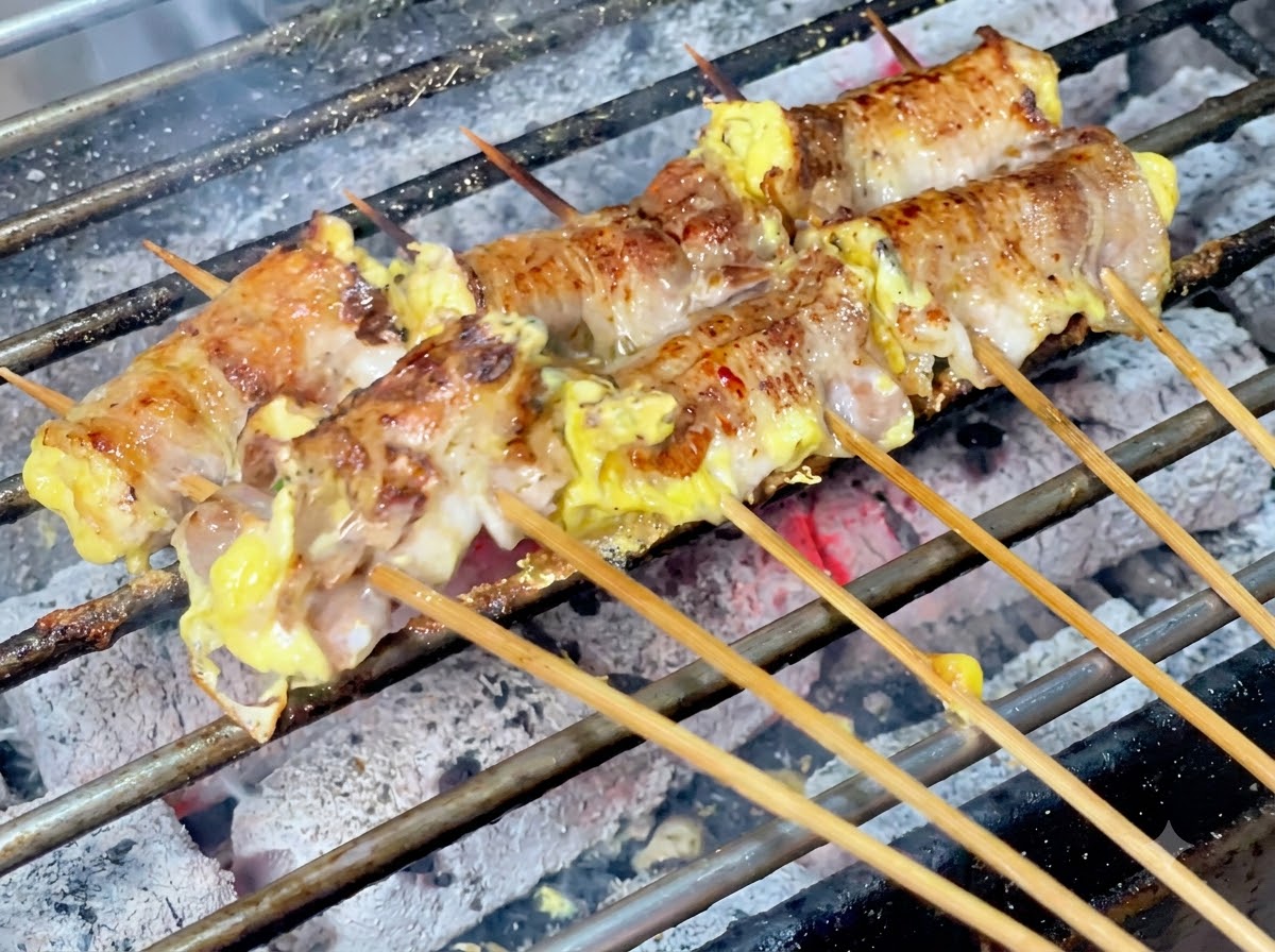 炭火焼きのジューシーな肉巻きにチリパウダーが均等に振りかけられている様子。