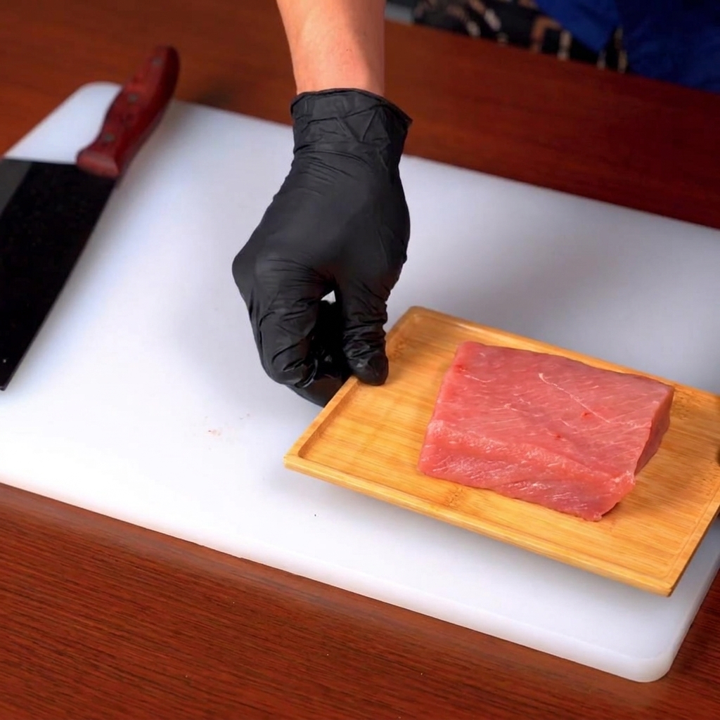 白いまな板の上で、生の豚ロース肉のかたまりを切っている様子。