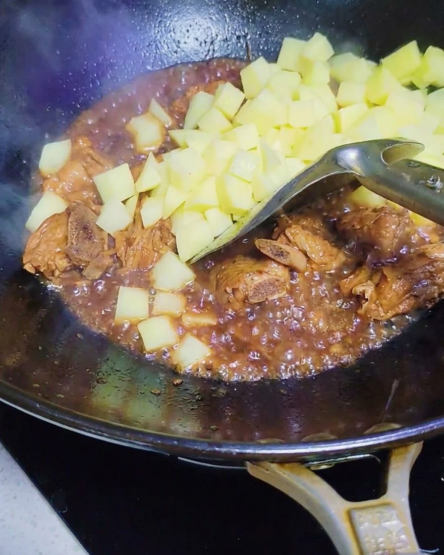 味付けされたスペアリブとソースが入った中華鍋に加えられている、生の角切りじゃがいも。