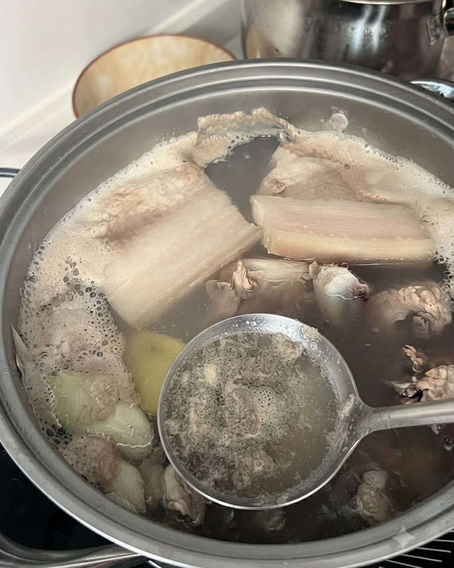 豚スペアリブの入った沸騰した鍋から、穴あきお玉で灰汁や不純物をすくい取っている様子。