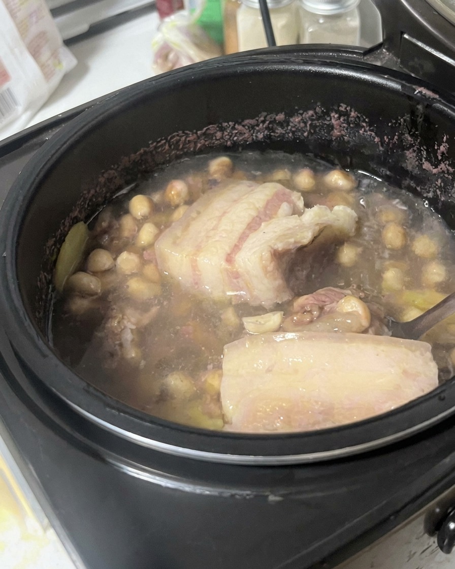 スープの入った鍋の中で、スプーンを使って豚バラ肉を持ち上げ、状態を確認している様子。