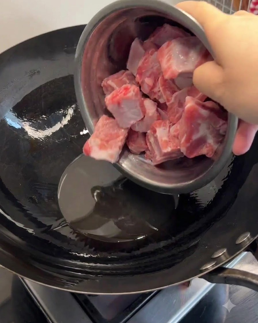 熱した中華鍋の中で溶けたラードに豚スペアリブが加えられ、表面がきつね色に焦げ目がつくまで炒められている様子。