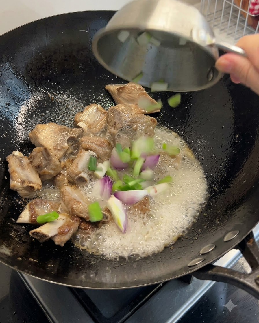 中華鍋の中のスペアリブと一緒に、青ネギ、生姜、干し海鮮の食材が投入されているところ。