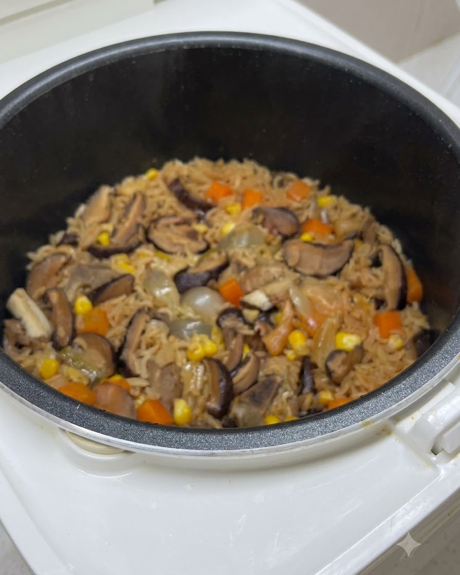 炊飯器の釜の中で、きのこ、ニンジン、コーンが混ざり合った炊き上がり直後のご飯。