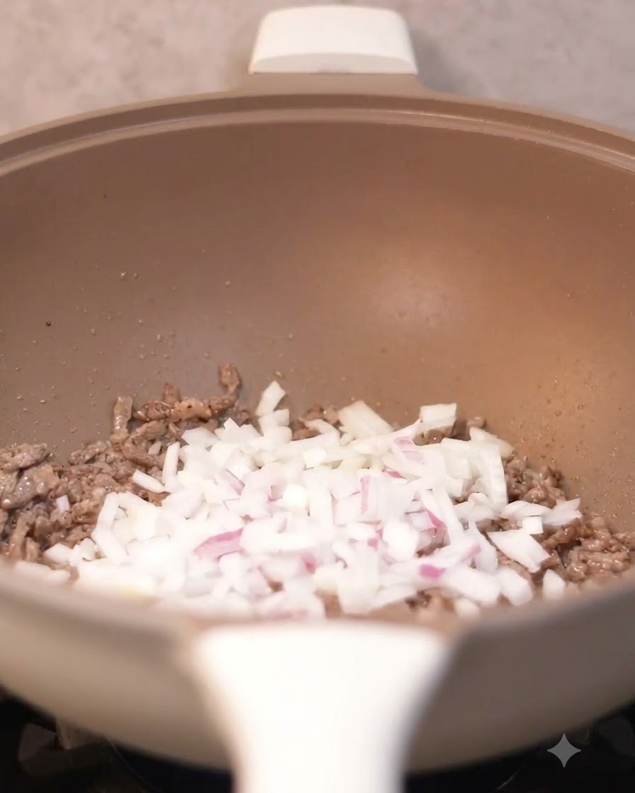 調理中の牛肉が入った中華鍋に、みじん切りの玉ねぎが加えられている様子。