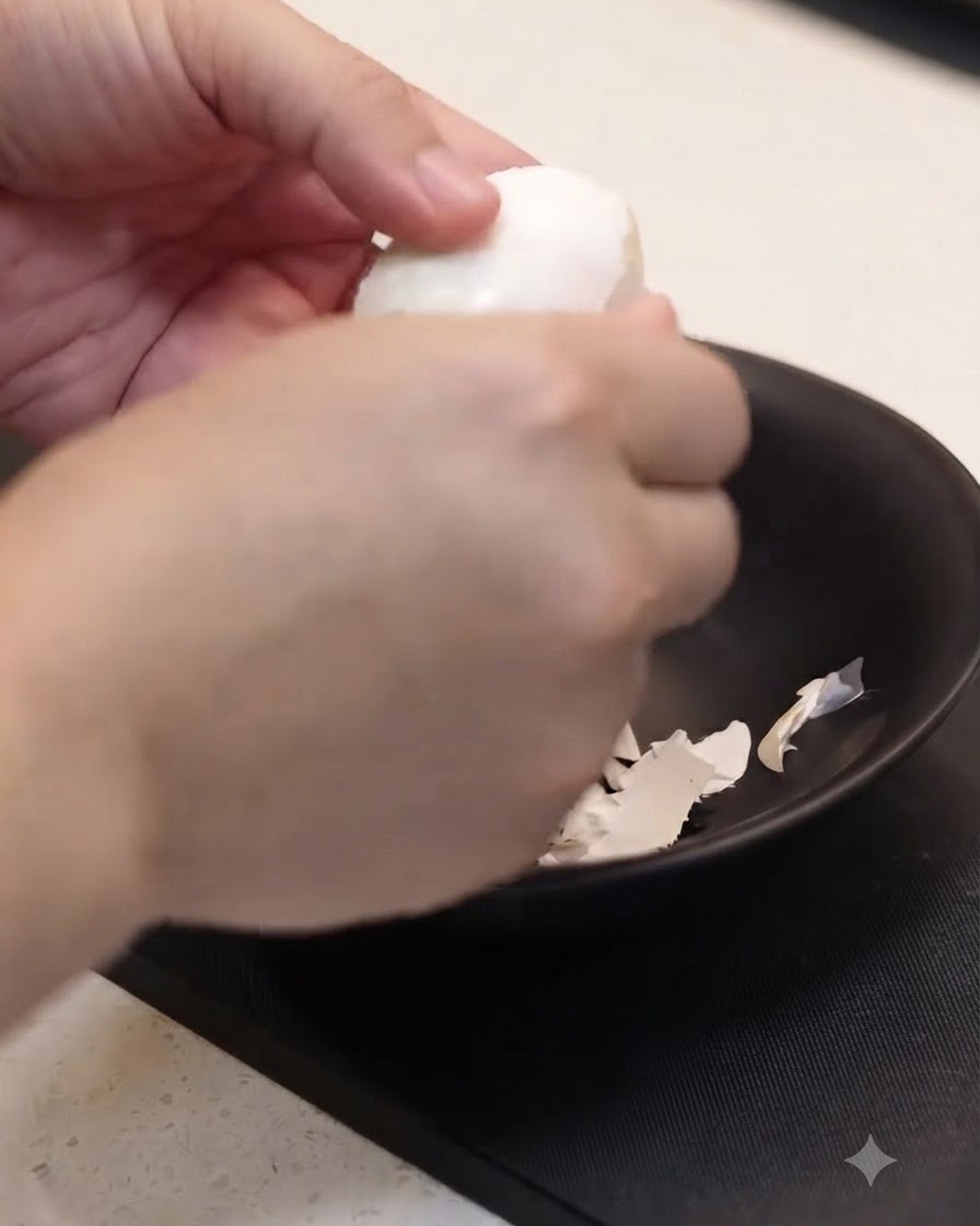 黒いボウルの上で、茹で上がった卵の殻を手で慎重にむいている様子。