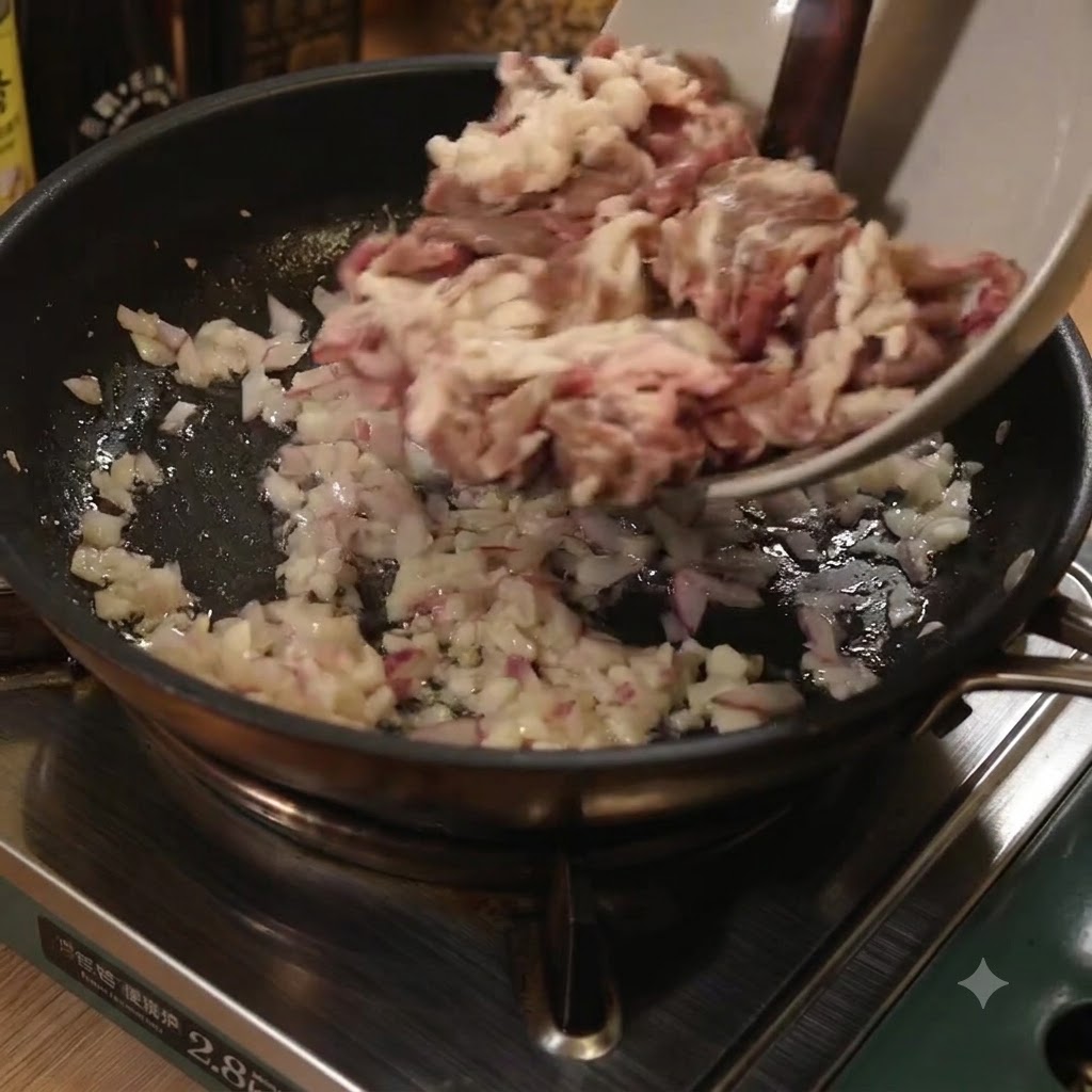玉ねぎとニンニクを炒めたフライパンに、ボウルから牛肉の細切りを入れている様子。