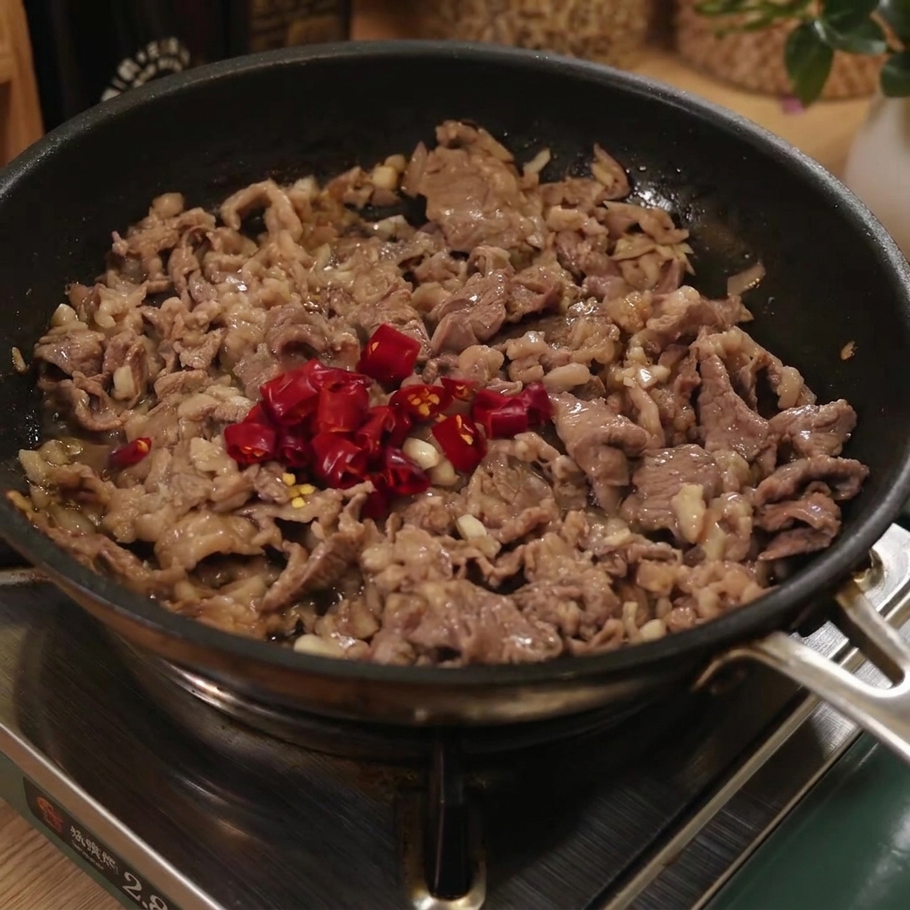 牛肉と赤唐辛子の入ったフライパンに、茹で上がったスパゲッティを入れている様子。