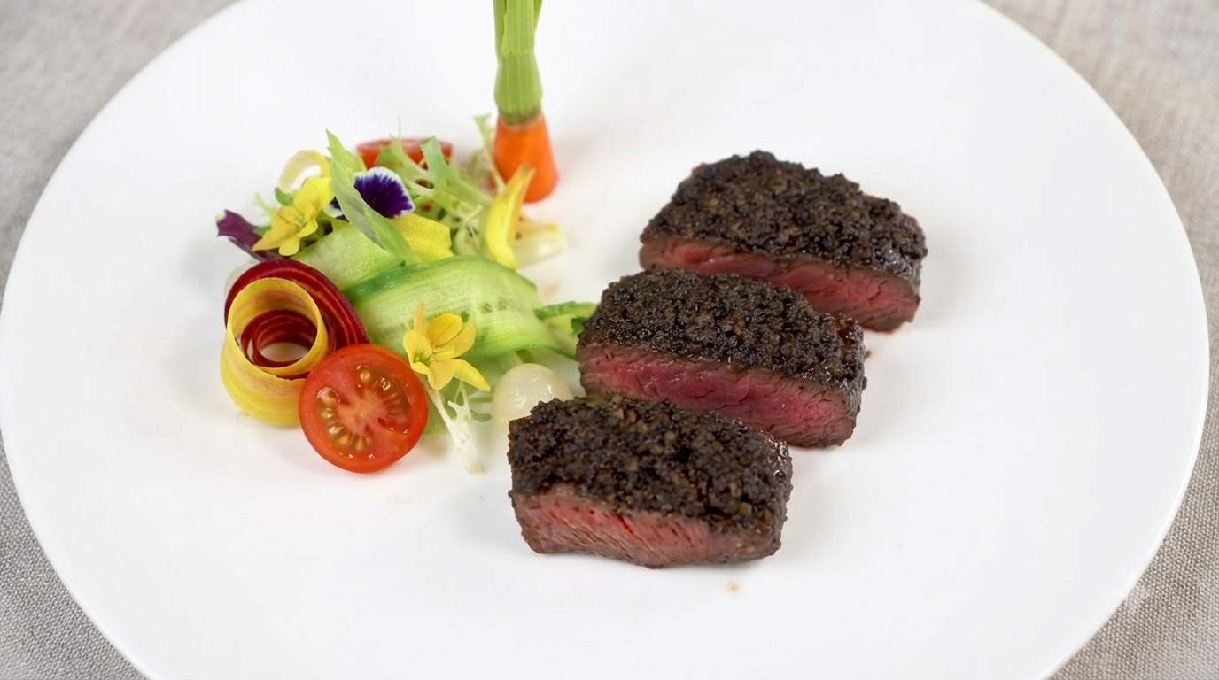 豊かな黒トリュフペーストをトッピングし、新鮮な野菜の付け合わせを添えた、ミディアムレアの厚切りステーキ3切れ。
