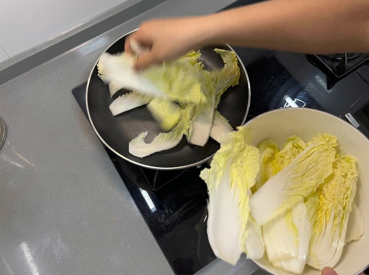 フライパンの底に、白菜の葉を敷き詰めて保護層を作っている様子。
