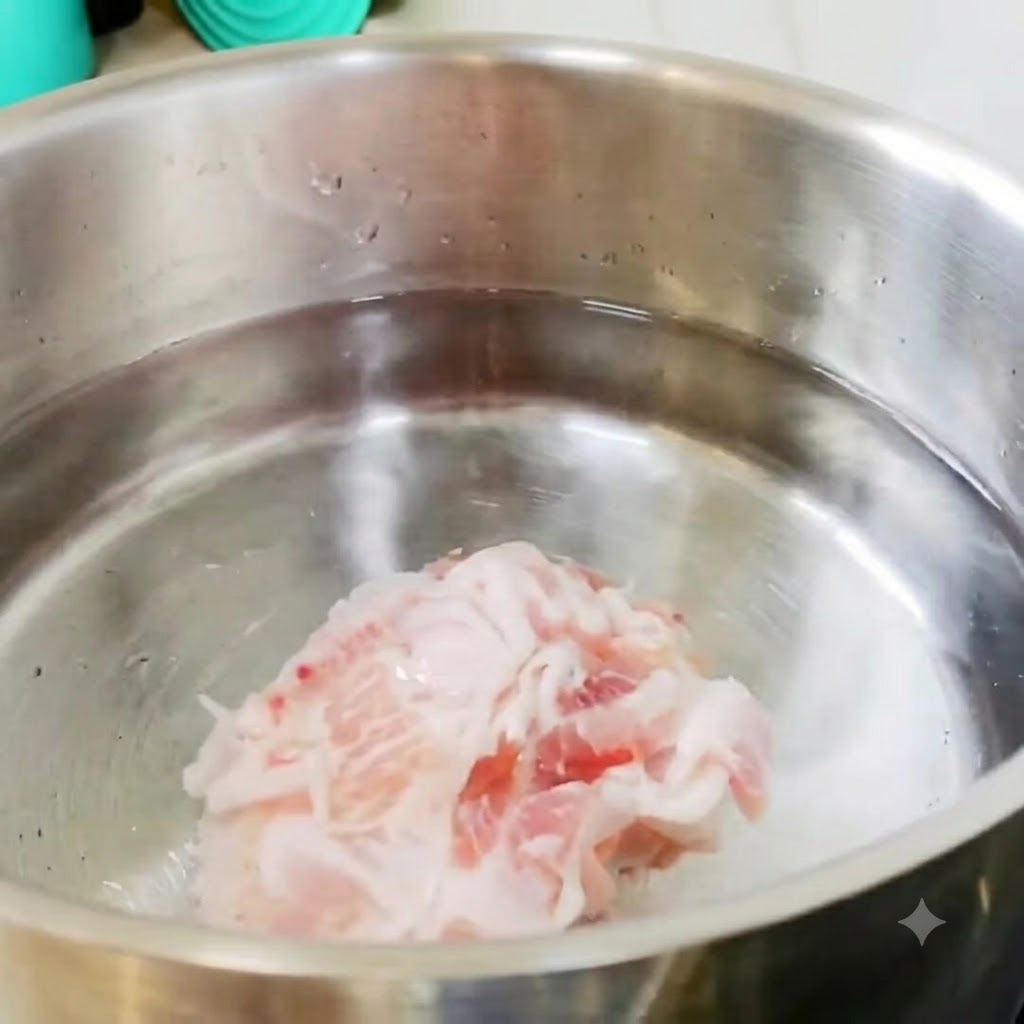 スライスした豚バラ肉とじゃがいものピースが、コンロ上の冷たい水が入ったステンレス製の鍋に入っている様子。