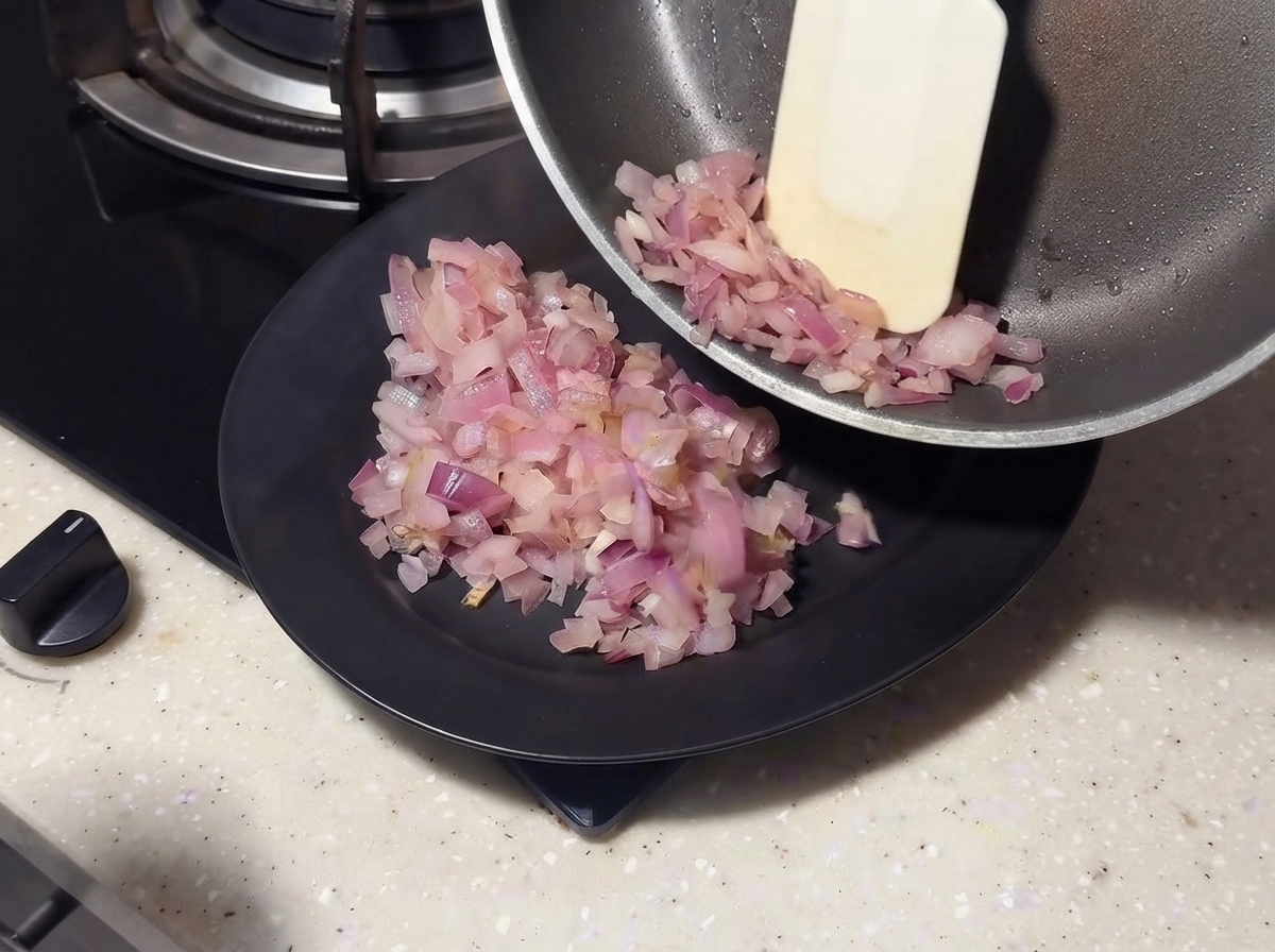 スパチュラを使って、フライパンから炒めた玉ねぎを黒い皿に滑らせている様子。