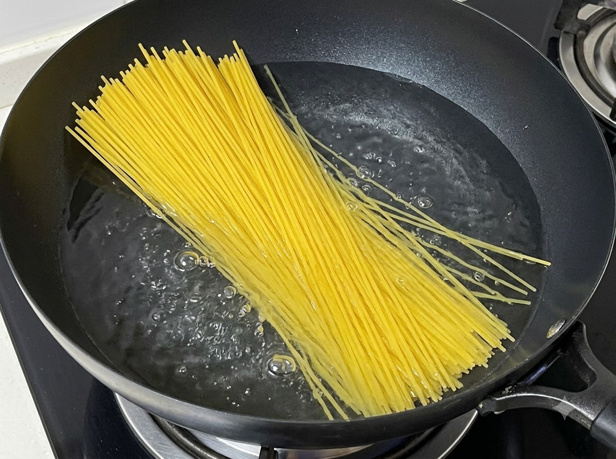 沸騰したお湯の入った鍋に、束ねた乾燥スパゲティを入れている様子。