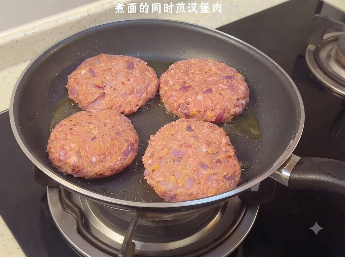 コンロの上のフライパンで、4つの生ハンバーグがジューシーに焼かれている様子。