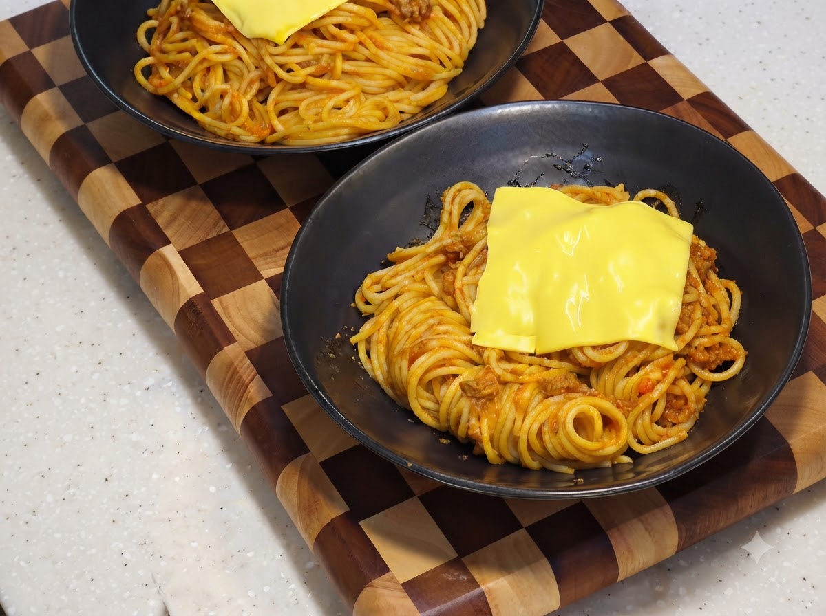黒いサービングボウルの中で、スパゲティの上のチーズがとろけている様子。