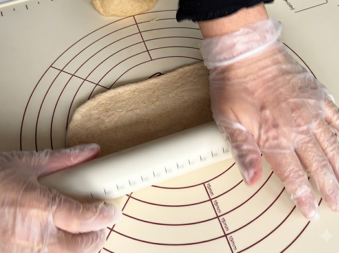 シリコンマットの上で、麺棒を使って全粒粉の生地を平らに伸ばしている様子。