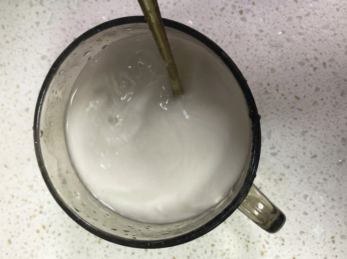 ガラスのコップの中でスプーンを使って水とサツマイモ澱粉の混合物が混ぜられている様子。