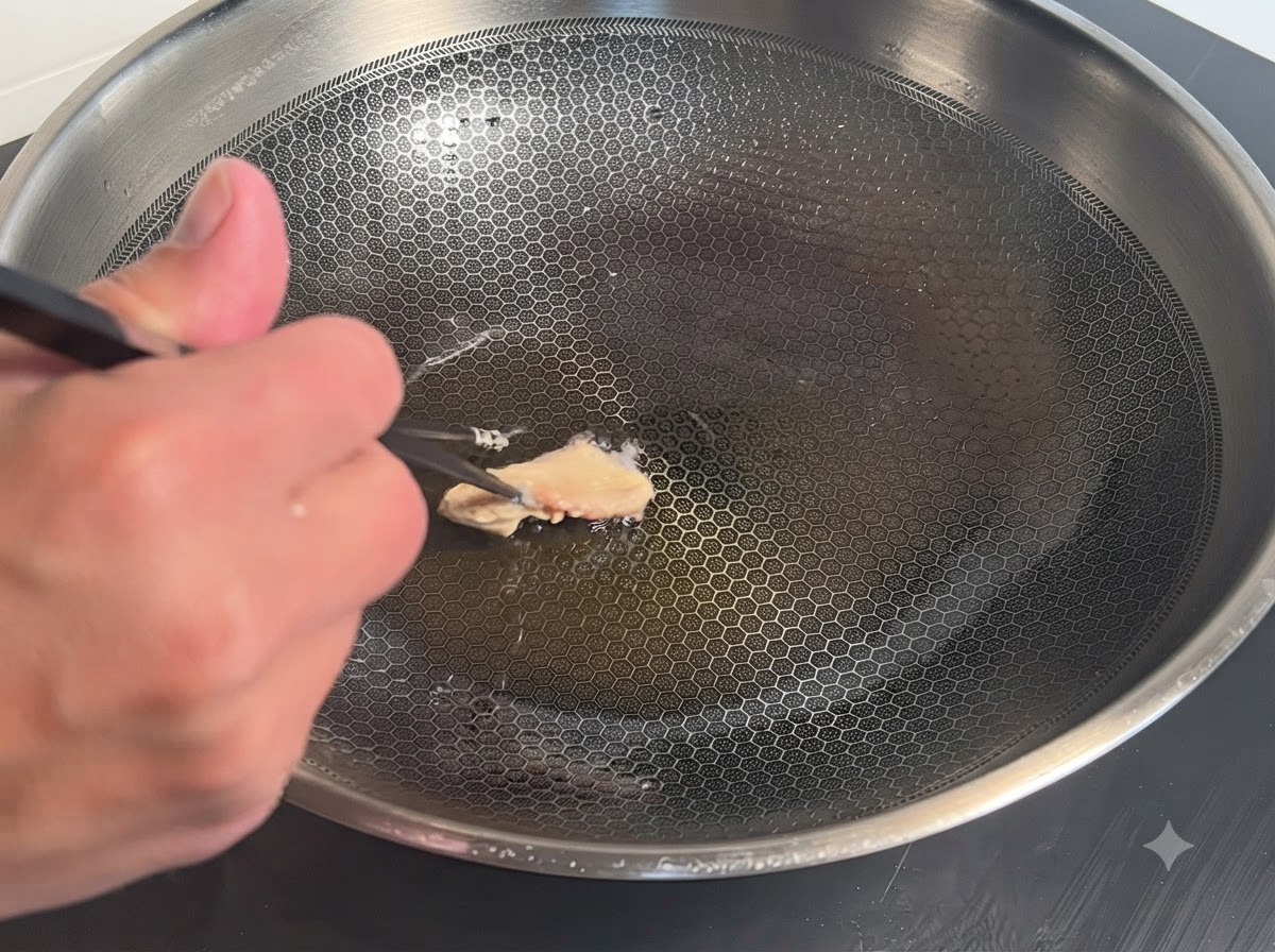 衣をまとった鶏肉の塊を、油の入った熱い金属の中華鍋に箸で入れている様子。