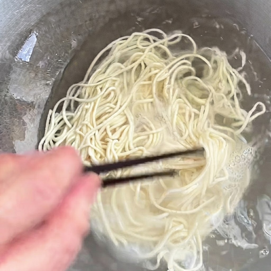 箸でかき混ぜながら鍋で調理されている麺。