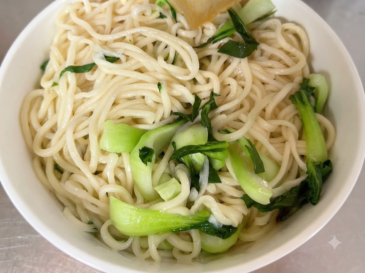 白い盛り付け用の器にきれいに配置された、茹でた麺と新鮮なチンゲン菜。