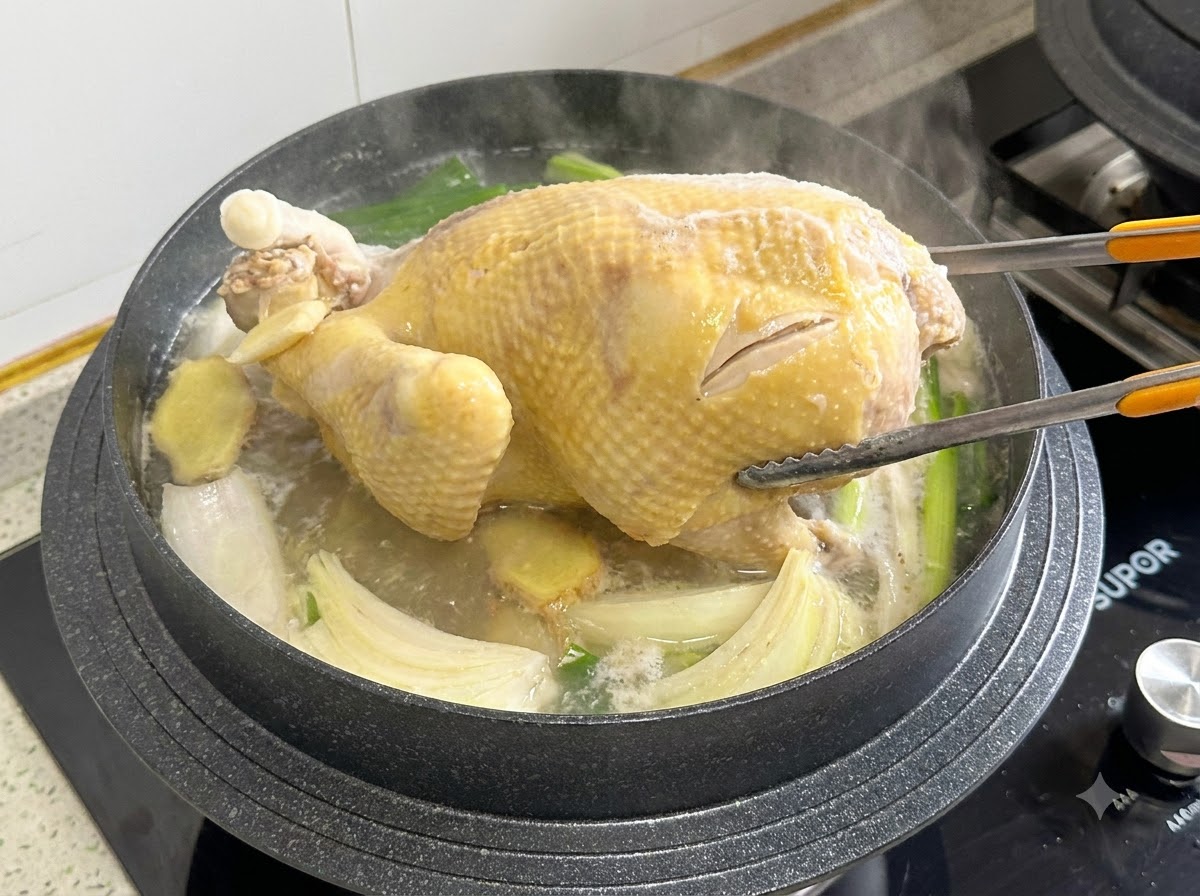 煮込んでいる鍋の中で、調理用トングを使って丸鶏をひっくり返している様子。