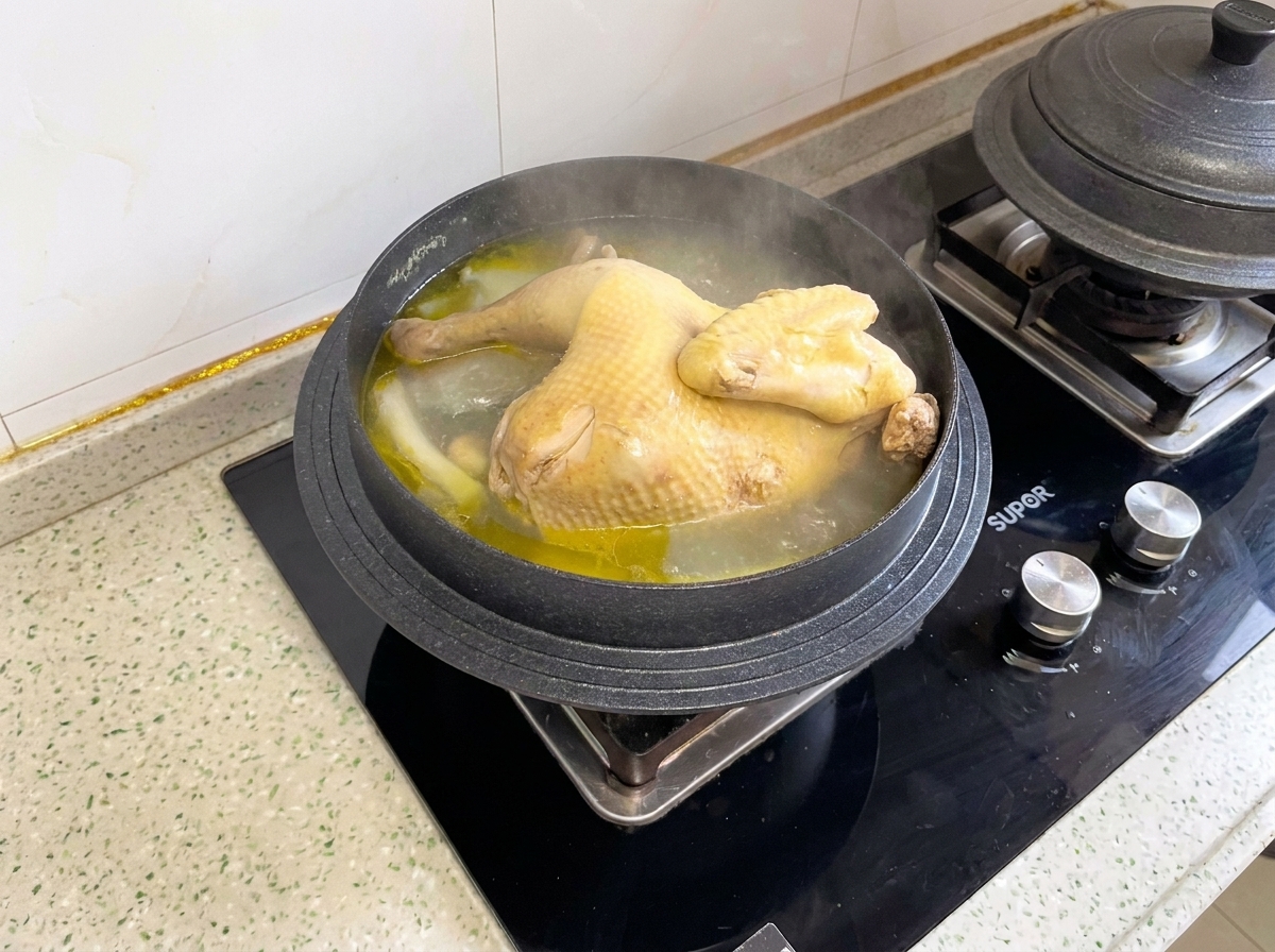 調理中の鍋の中で、柔らかく煮込まれた丸鶏を切り分けている様子。