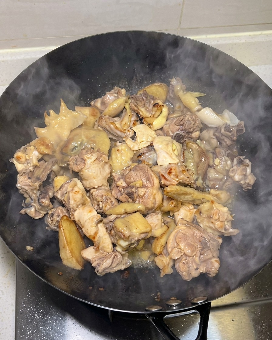 きつね色に焼き目がついた鶏肉が、湯気を上げながら中華鍋で調理されている様子。