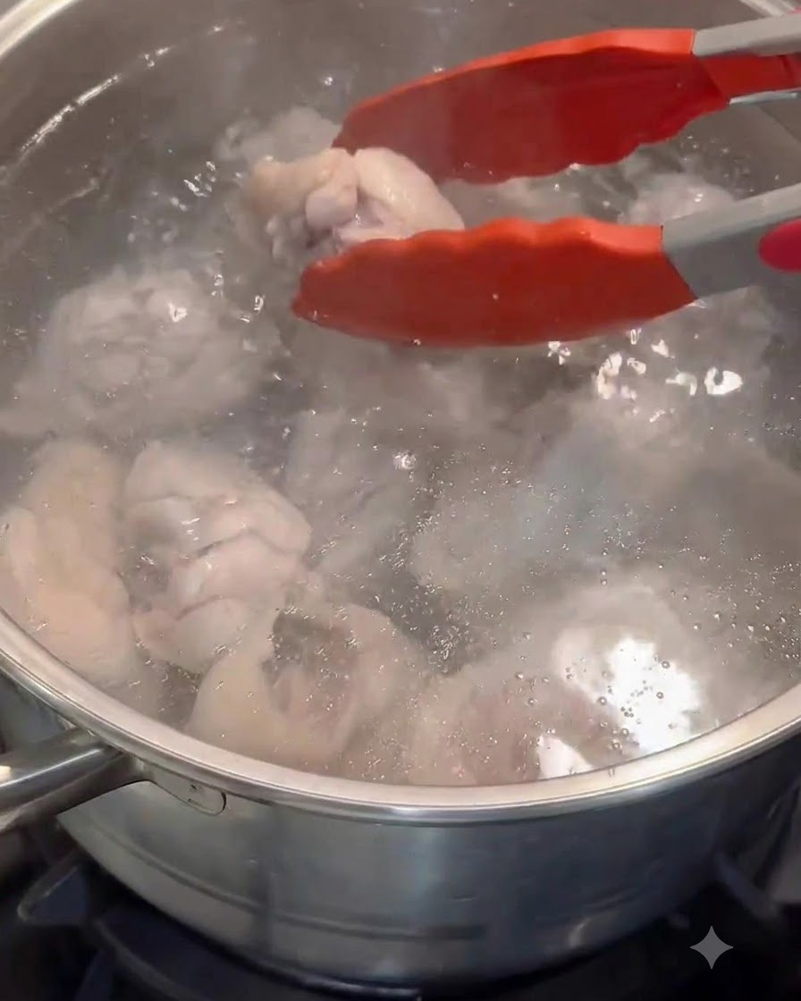 赤いトングで、下茹でした鶏肉を新しいお湯の入した鍋に移している様子。