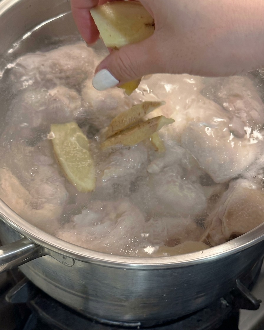 鶏肉の入った沸騰した鍋に、手で生姜のスライスを投入している様子。